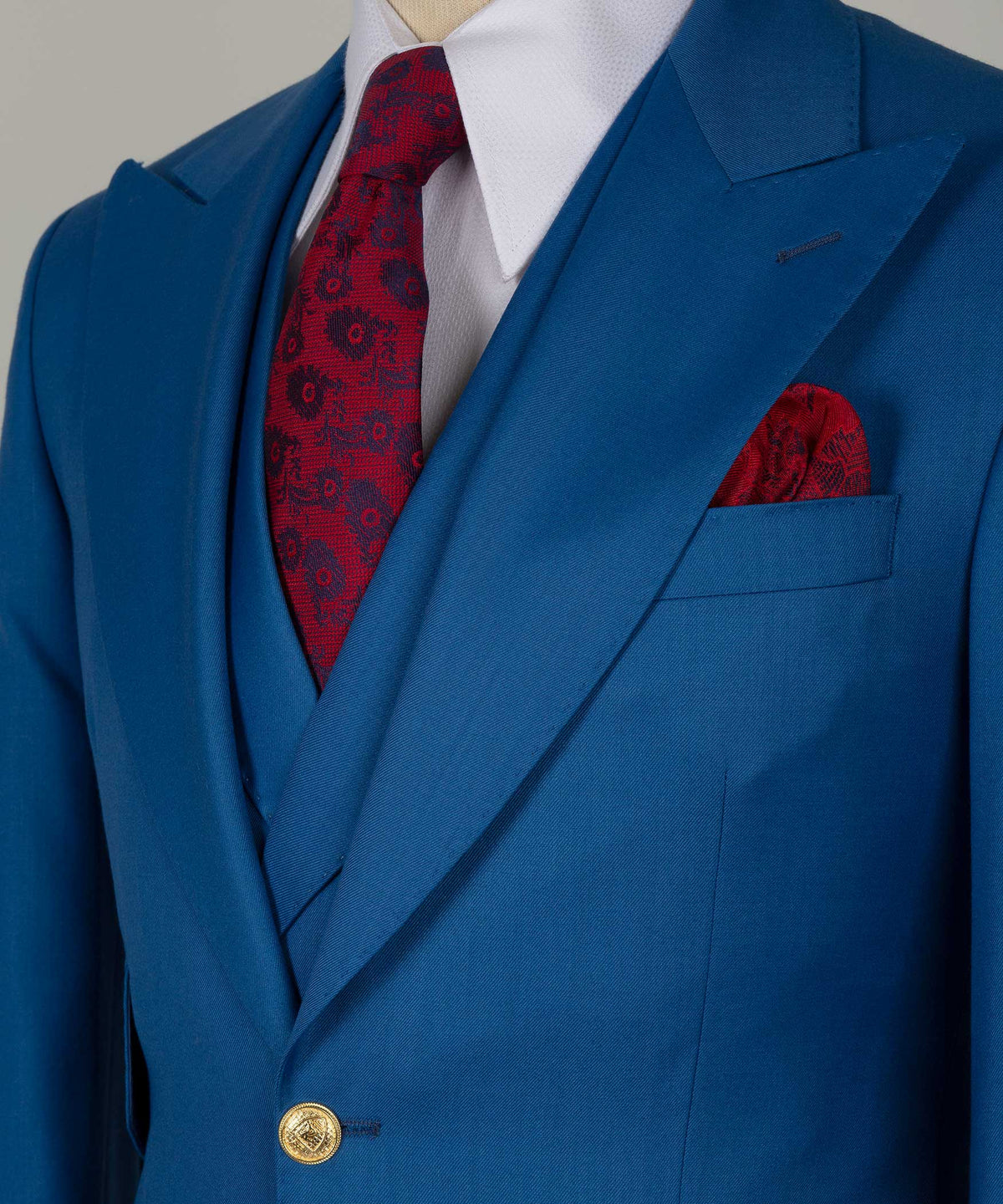 Close-up of blue suit lapel with gold button, red patterned tie, and red pocket square