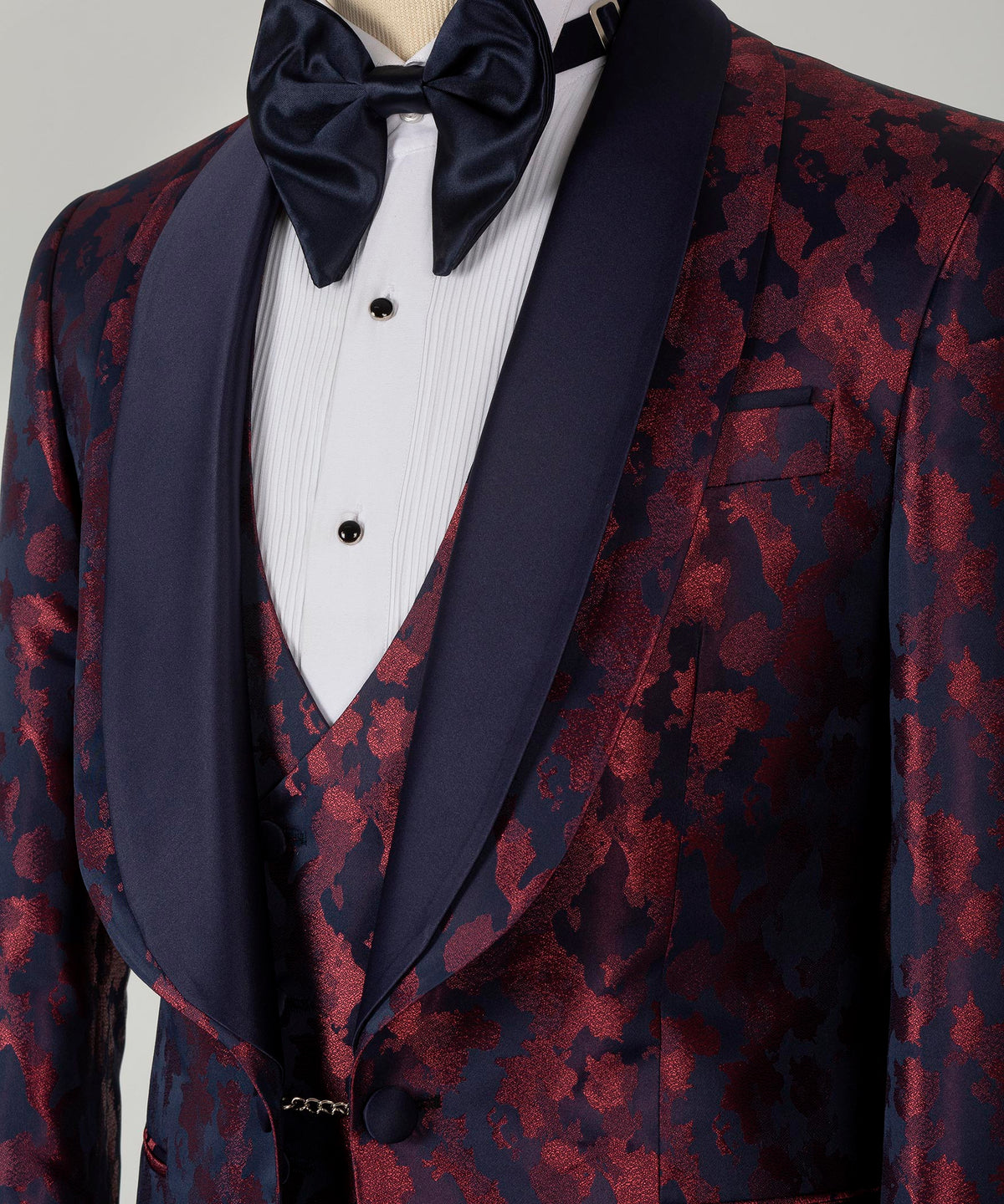 Tuxedo bow tie and dark lapels over burgundy patterned vest, satin sheen