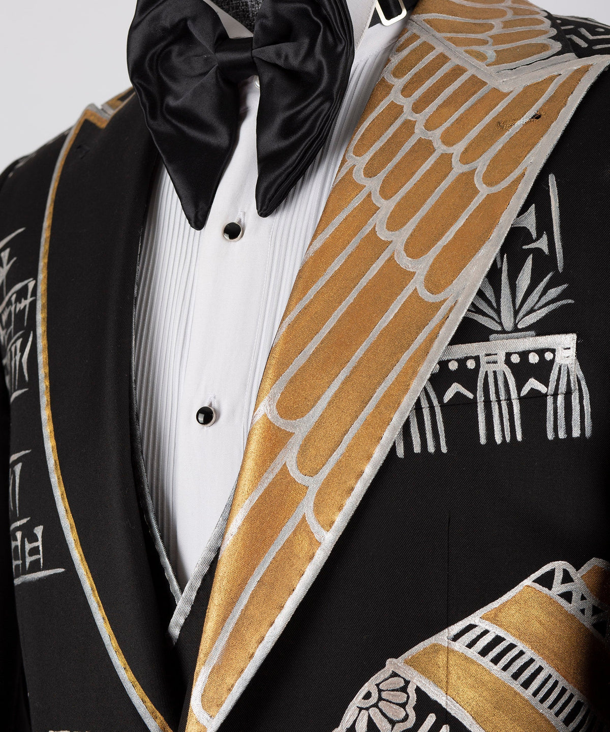 Close-up of black tuxedo lapel with gold embroidered trim, white shirt and bow tie