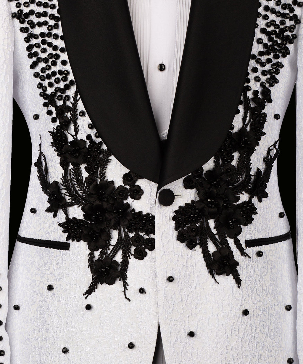 Close-up: white tuxedo jacket front with black floral appliqué and studded details