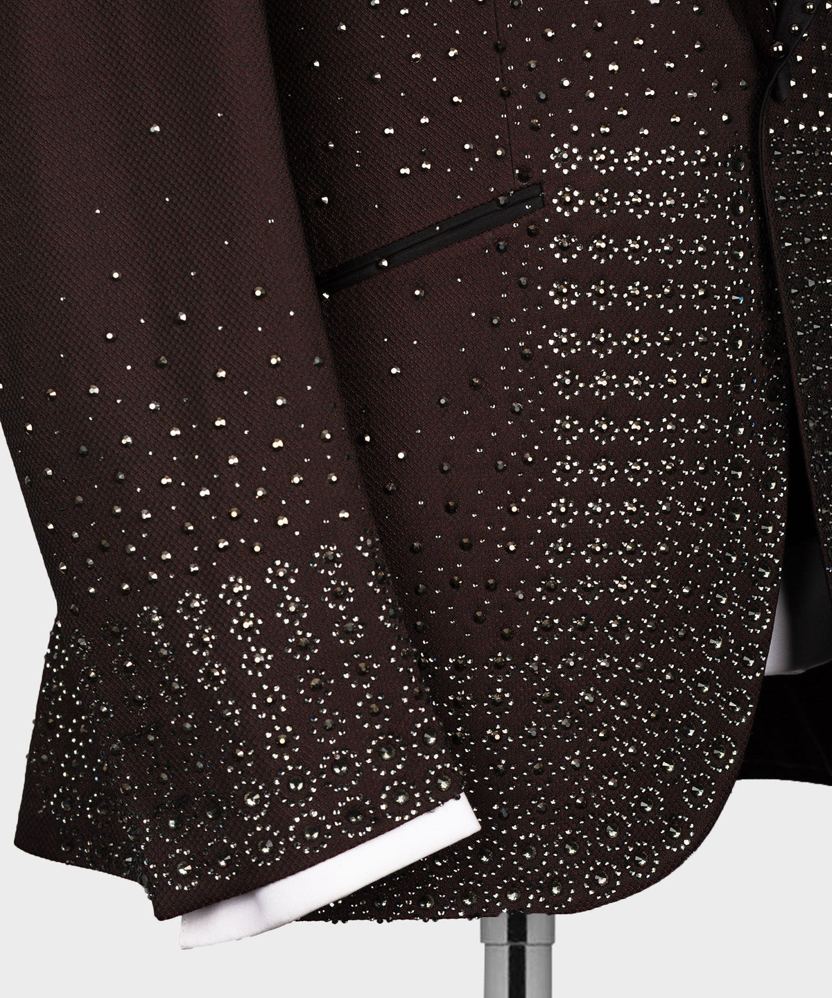 Close-up of burgundy tuxedo jacket hem with dense jeweled pattern and decorative trim