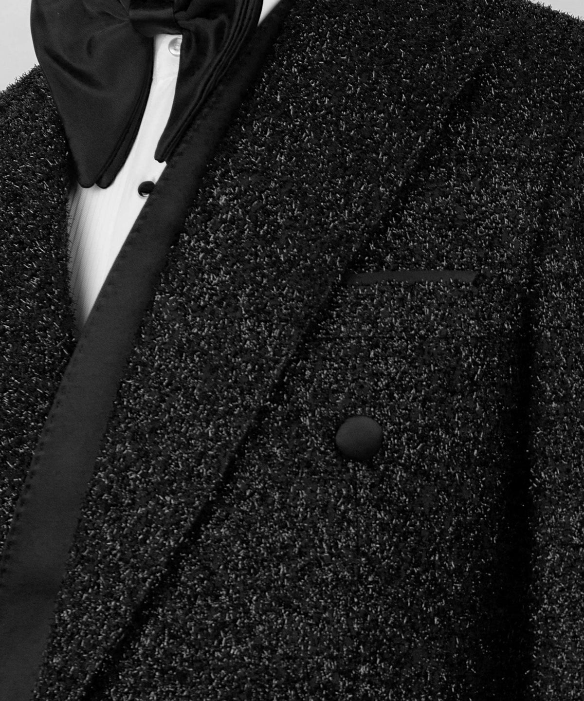 Close-up of black tuxedo jacket: shawl lapel, satin trim, and round button detail