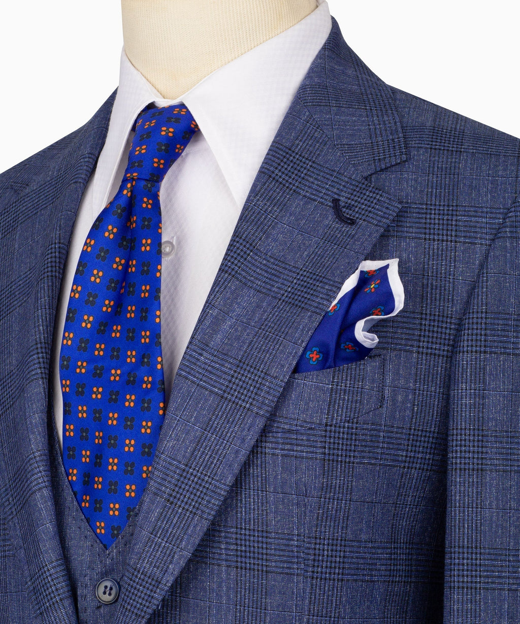 Close-up of blue plaid suit jacket lapel, pocket square, and matching patterned tie
